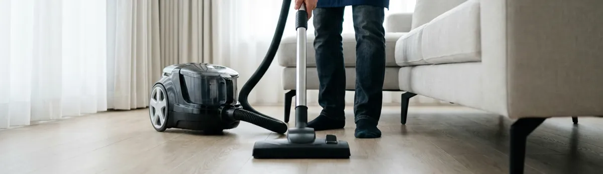 Professional house cleaner vacuuming a living room floor with a canister vacuum cleaner, Boston, MA.